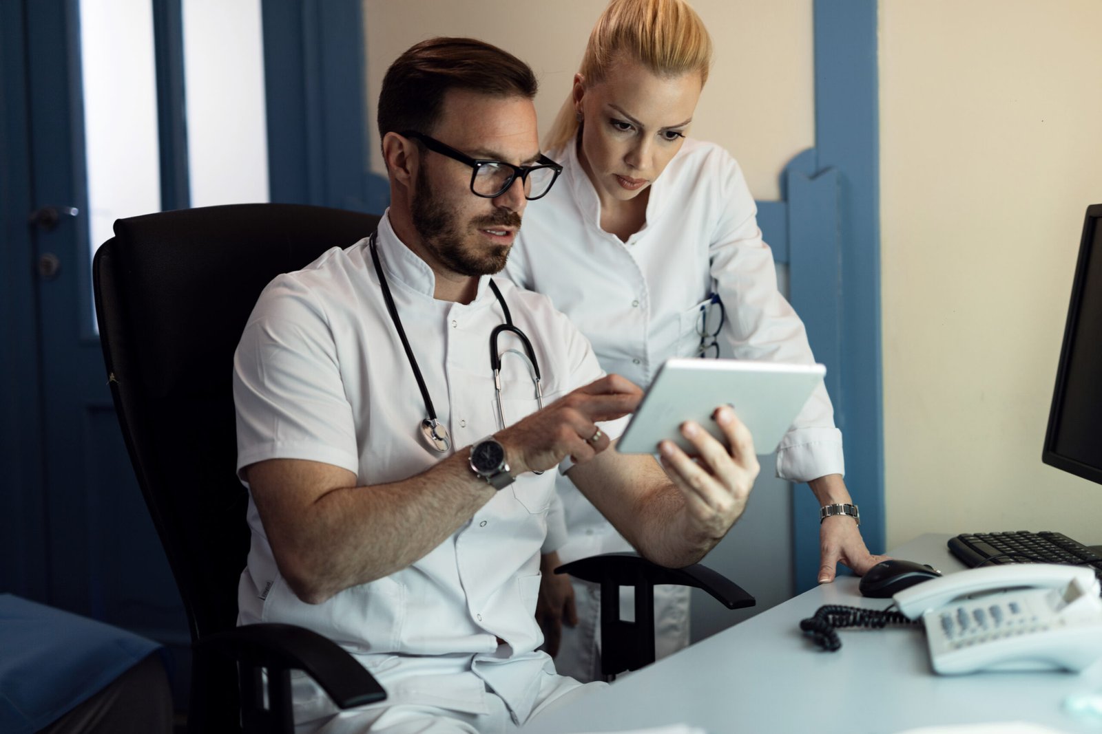 Two doctors analyzing medical reports on touchpad in the hospital.